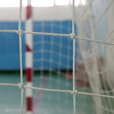 Nahaufnahme eines Handballtors mit weißem Netz und roten Markierungen auf der Wand in einer Sporthalle.